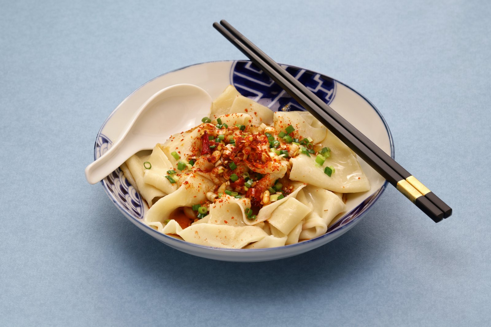 A bowl of wide biangbiang noodles topped with chili oil and chopped scallion