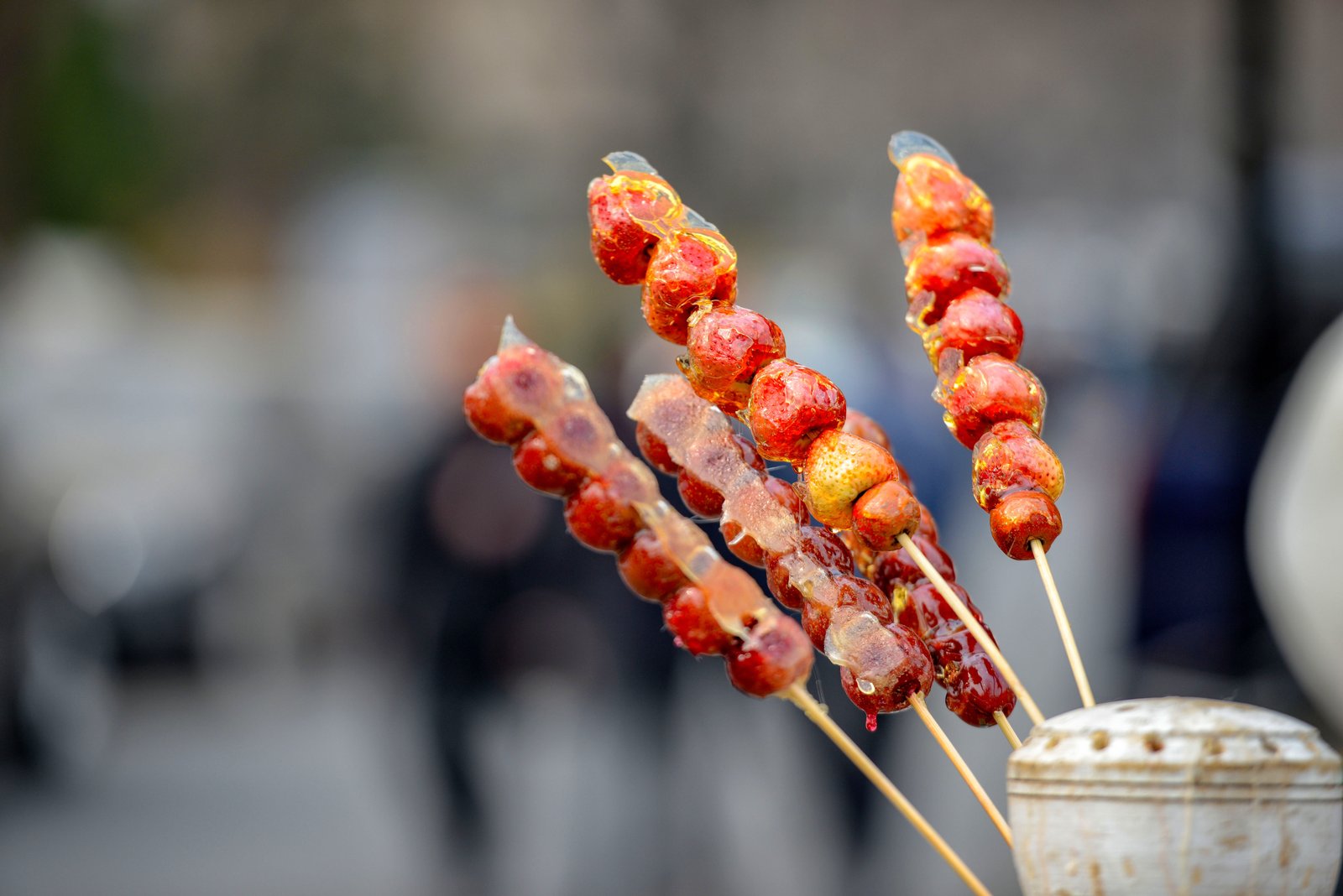 Skewers of tanghulu, candied hawthorn fruit on bamboo sticks, held up on a street