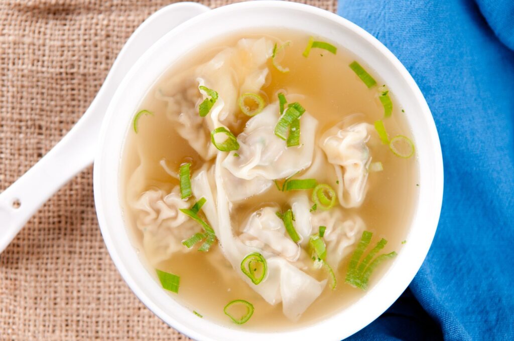 Wontons in clear broth with sliced scallions, served in a white bowl