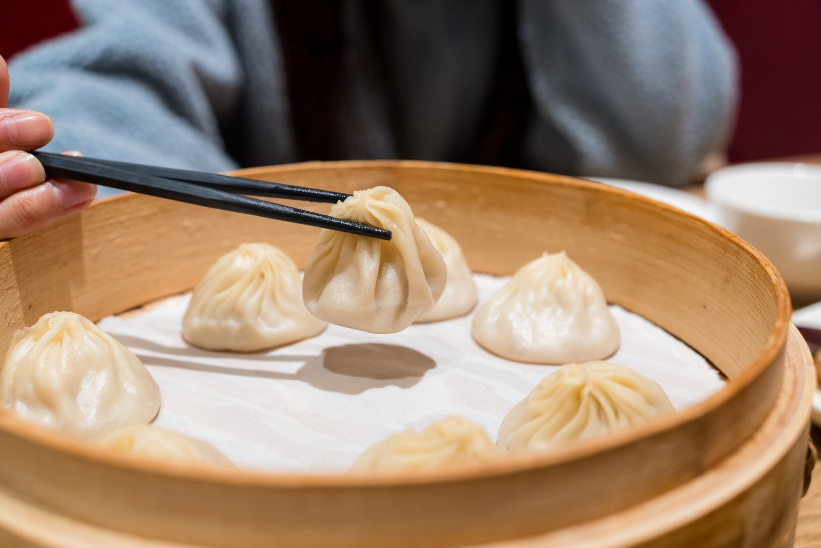 Chopsticks lifting a xiaolongbao from a bamboo steamer